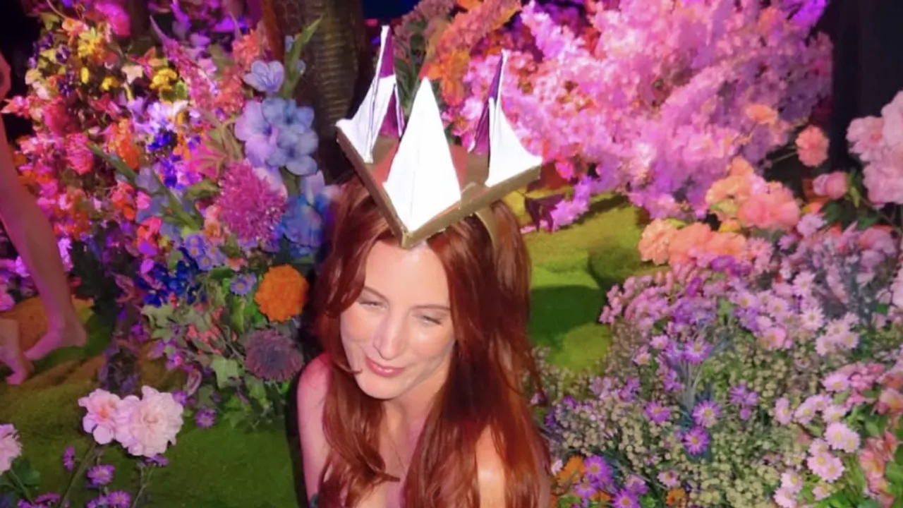 Arabella Rosier in a paper crown, surrounded by banks of pink, purple and orange flowers