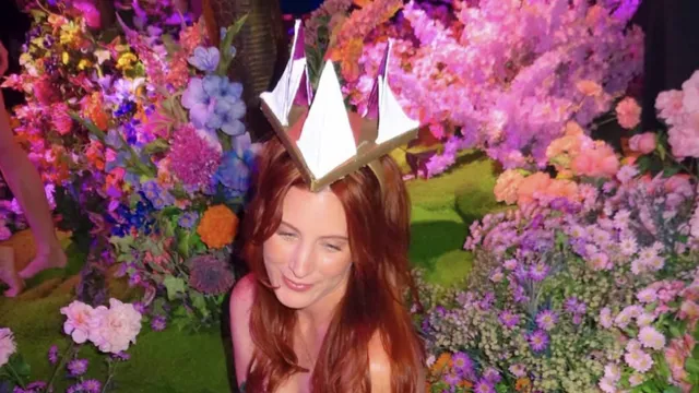 Arabella Rosier in a paper crown, surrounded by banks of pink, purple and orange flowers